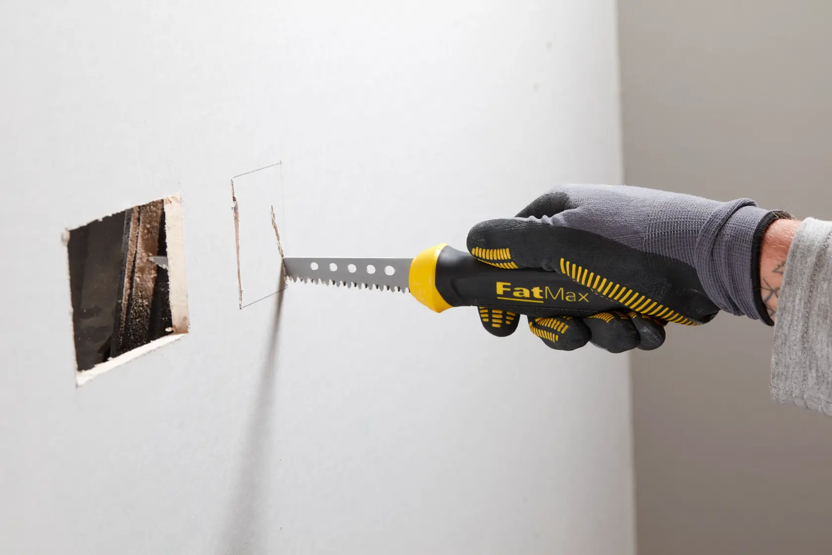 STANLEY 0-20-556 FatMax drywall saw cutting rectangular hole in wall, side angle, black and yellow handle.