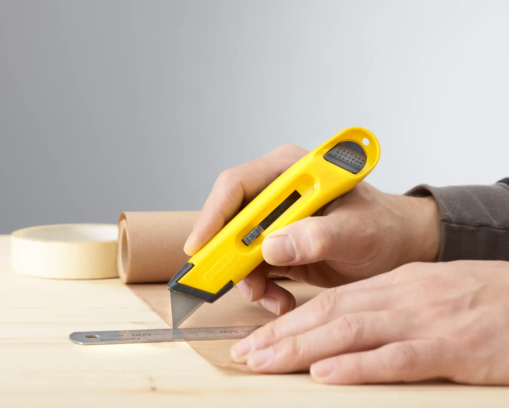 STANLEY 0-10-088 Cuttermesser mit gelbem Griff schneidet Papier neben einem Metalllineal auf Holztisch.
