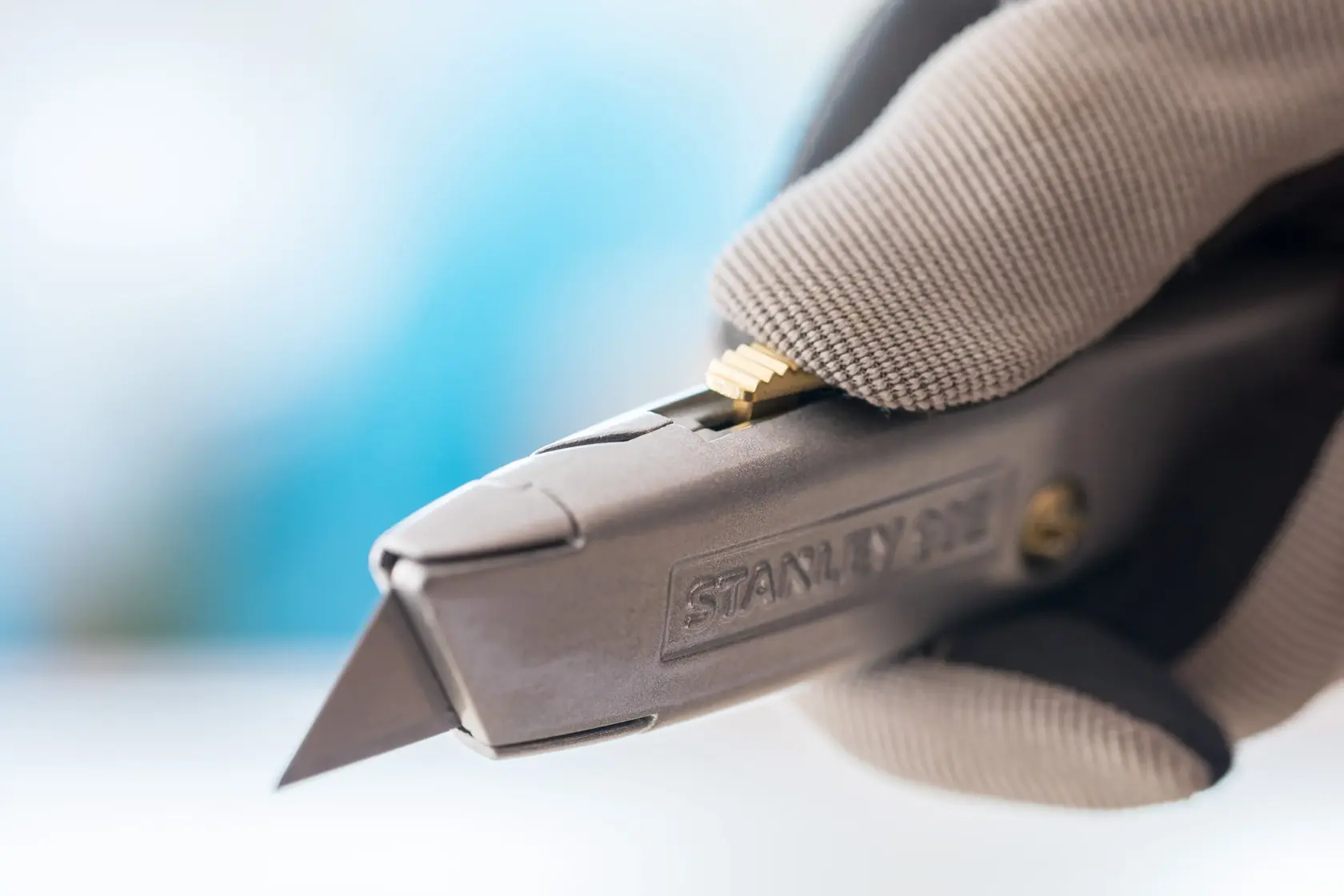 Close-up of STANLEY 0-10-099 utility knife in gloved hand, showing blade and textured grip.