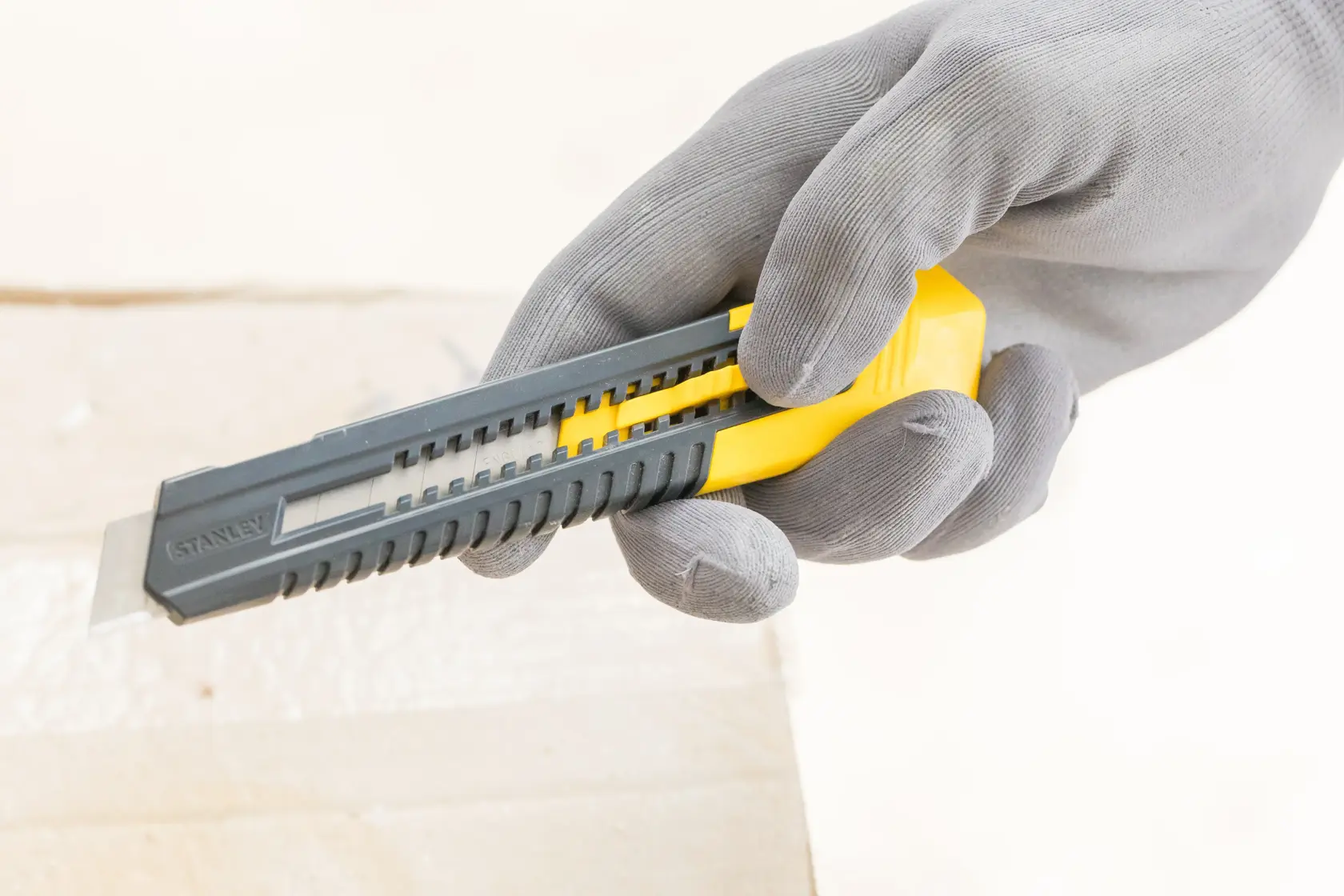 STANLEY 0-10-151 Universalmesser mit gelbem Schieber, gehalten von behandschuhter Hand, Nahaufnahme seitlich.