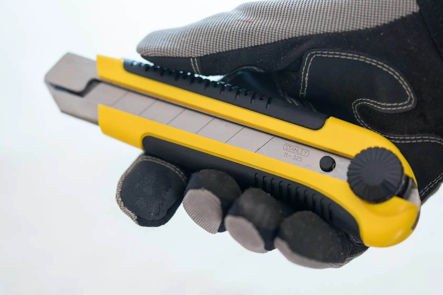 STANLEY 0-10-425 utility knife held in gloved hand, yellow and black retractable blade, side view.