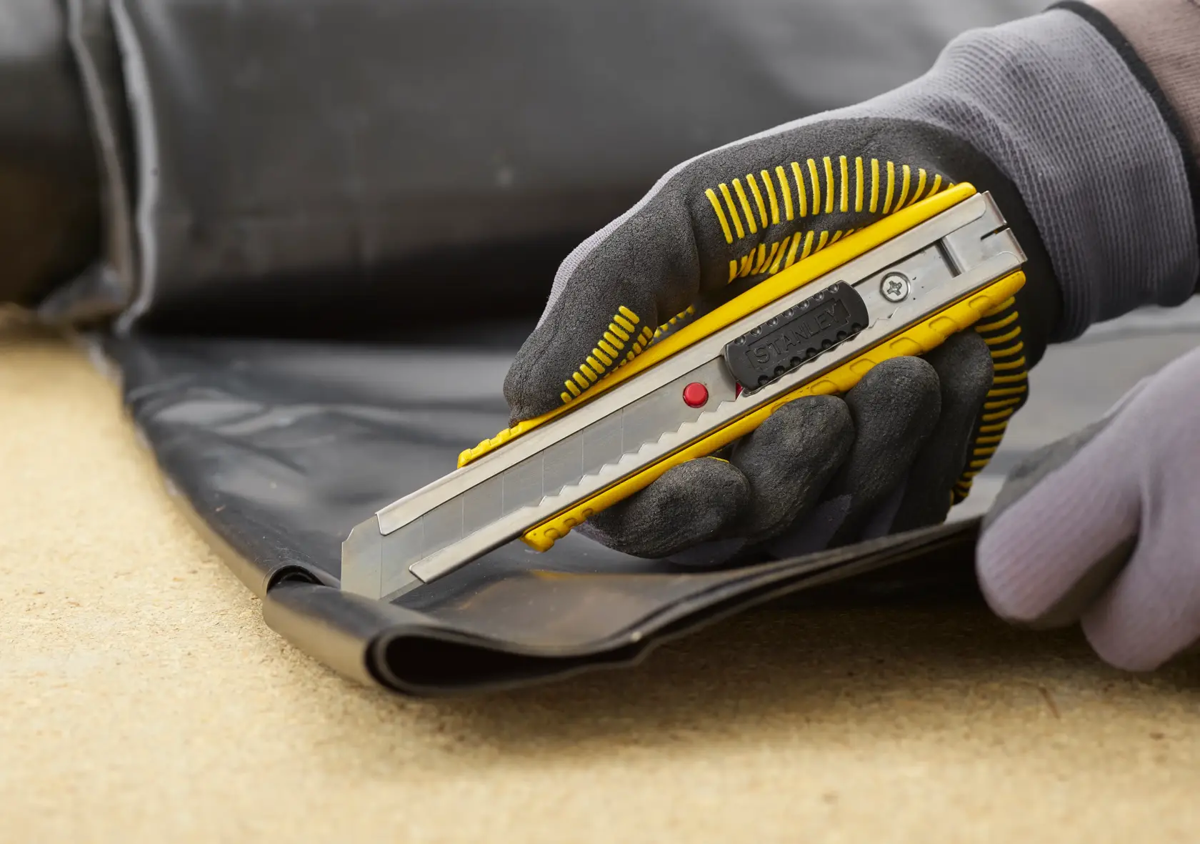 STANLEY 0-10-431 utility knife cutting black material, close-up of gloved hand using the tool.