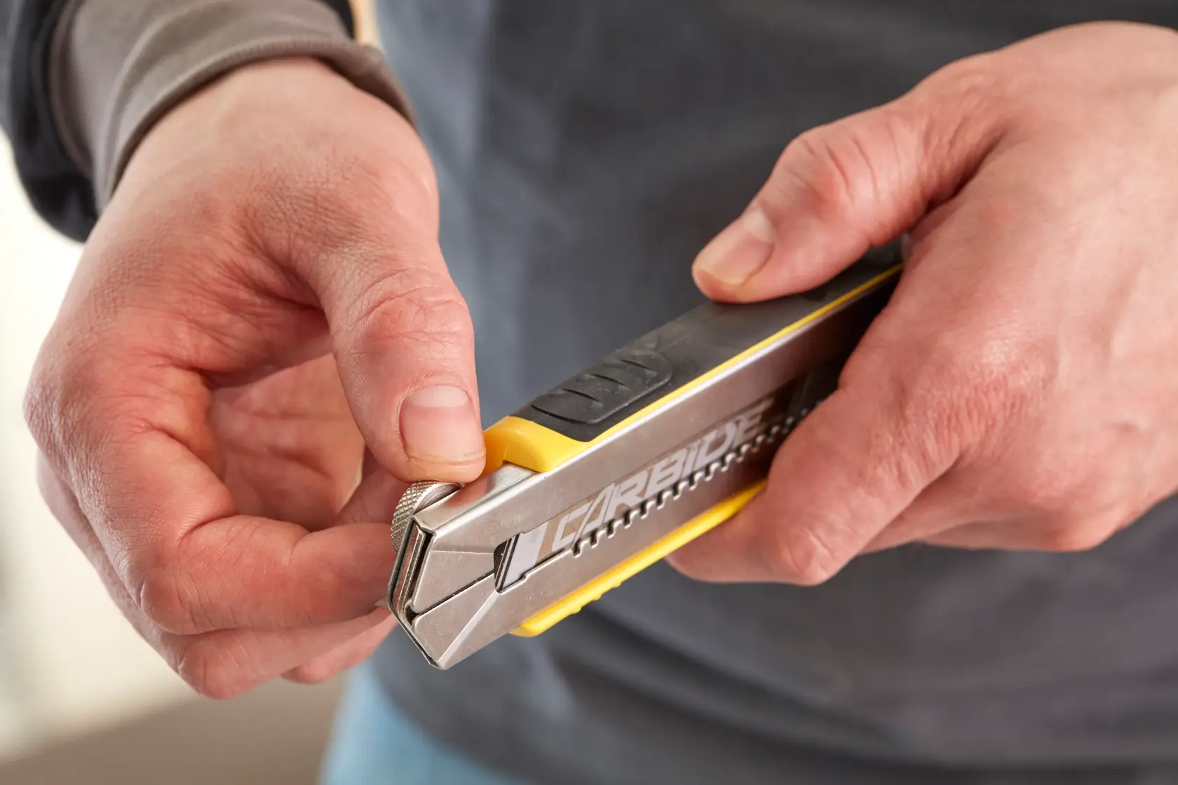 Photo of hands holding a STANLEY 0-10-481 snap-off utility knife, close-up angle showing blade adjustment.