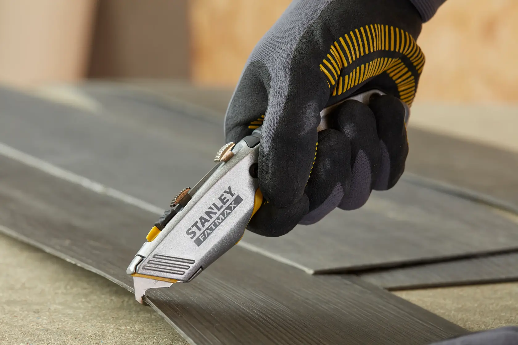 Stanley 0-10-789 utility knife held in gloved hand cutting dark laminate flooring.