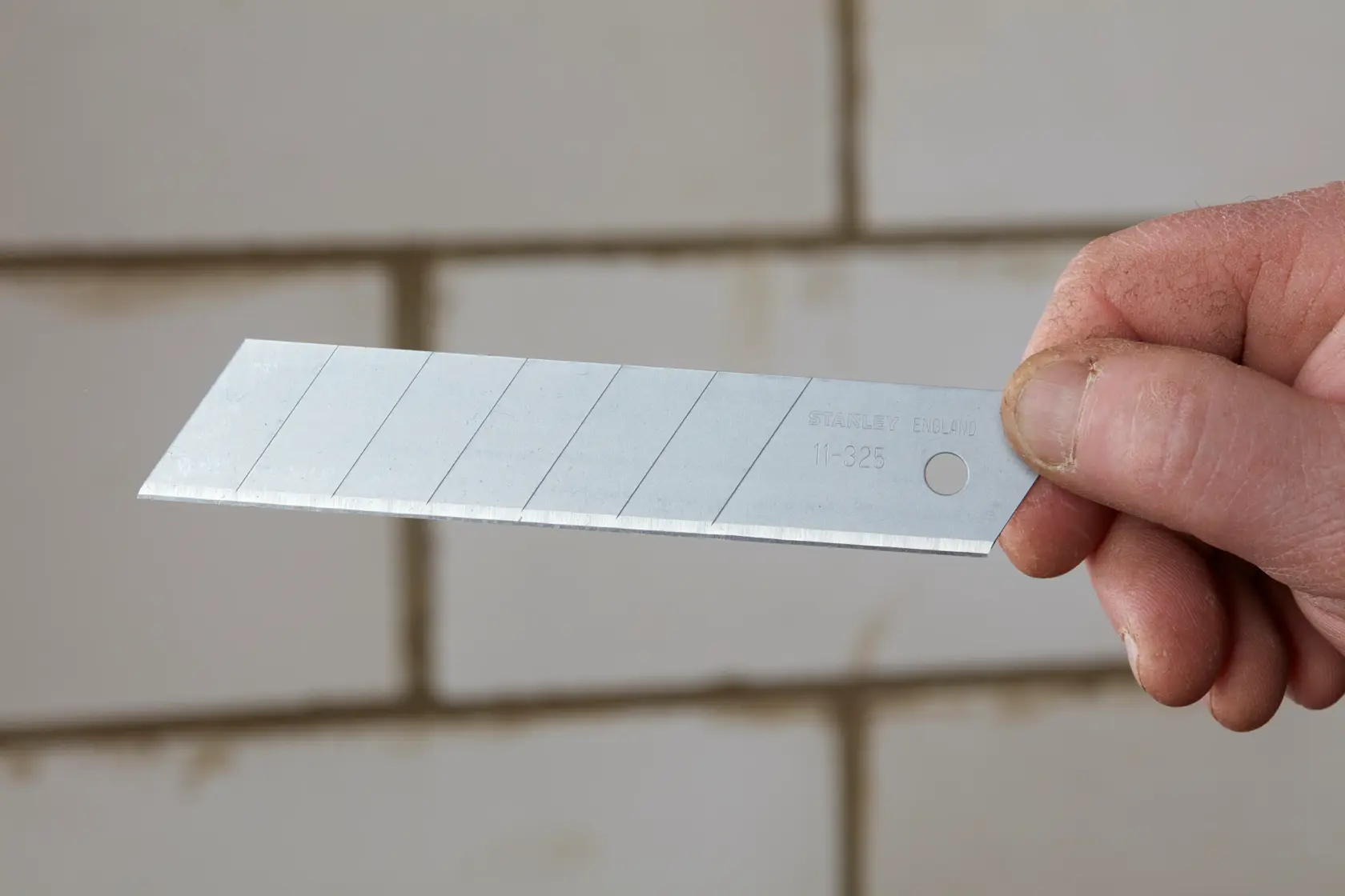 Photo of STANLEY 0-11-325 snap-off utility knife blade held by hand, silver color, multiple snap lines visible.