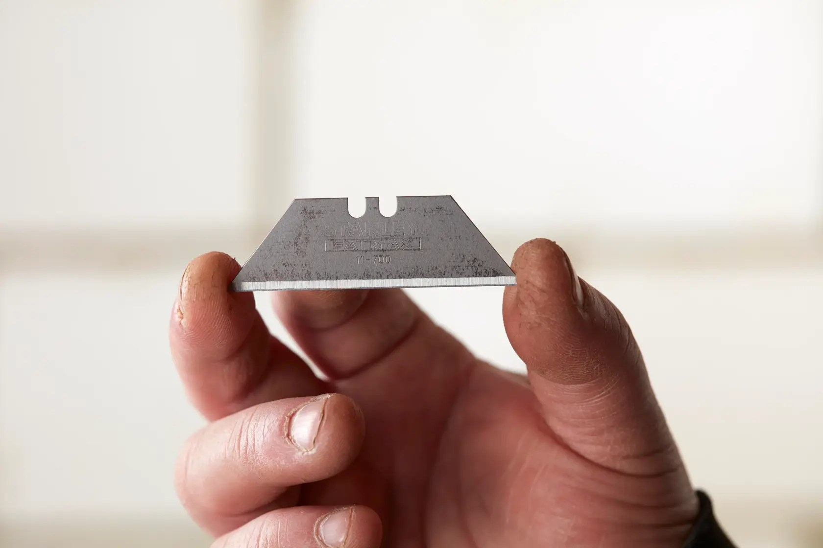Photo of STANLEY 0-11-700 utility knife blade held between fingers, showing sharp edge and notched design.