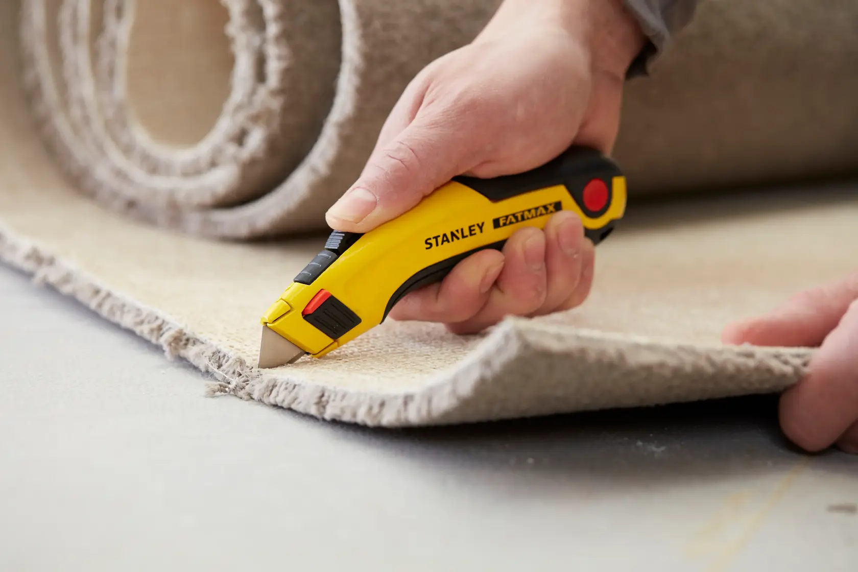 STANLEY 0-11-700 utility knife cutting carpet, close-up photo, yellow and black handle, FatMax series.