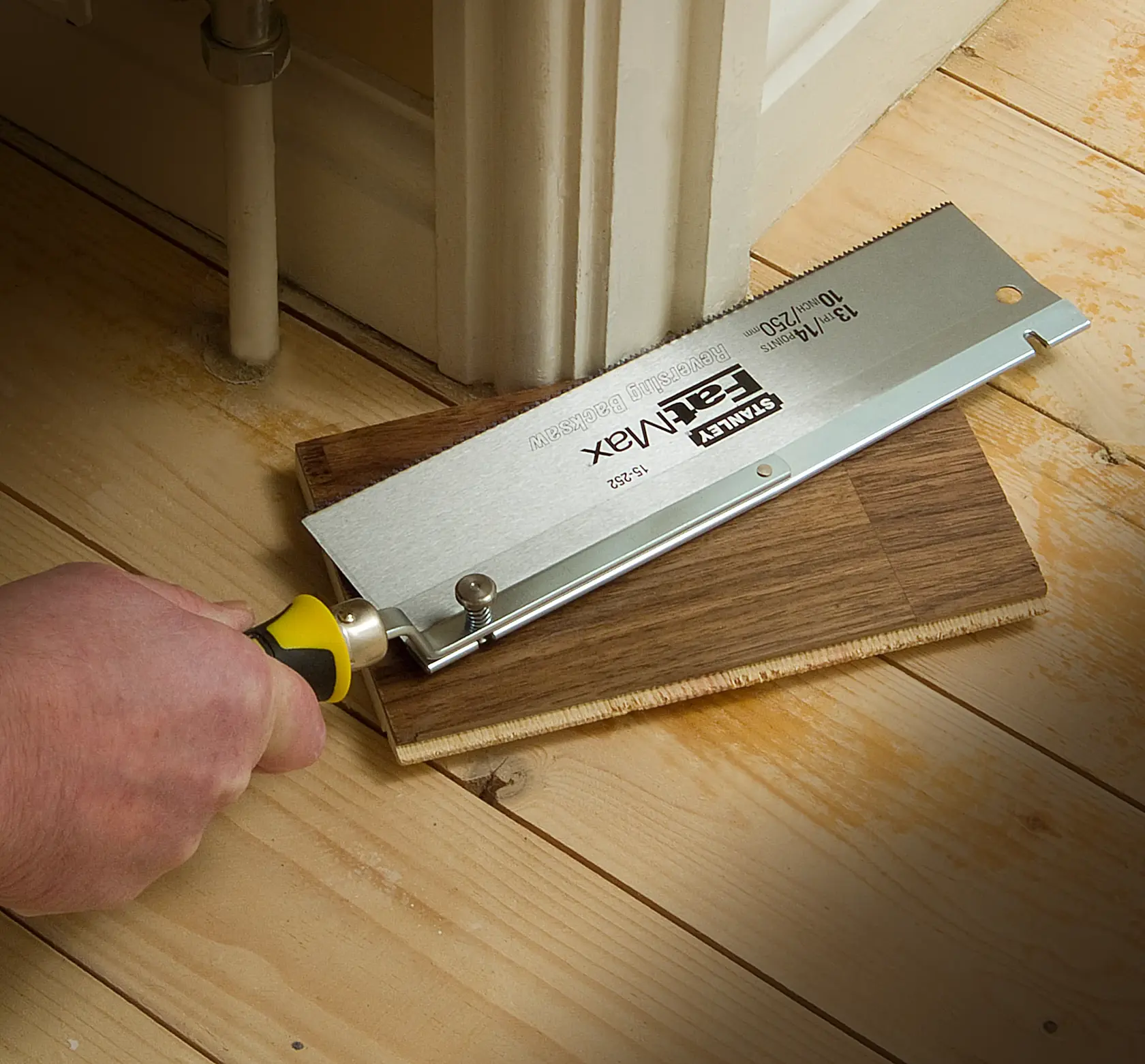 STANLEY 0-15-252 flush cut saw cutting laminate flooring near a door frame, close-up angle.