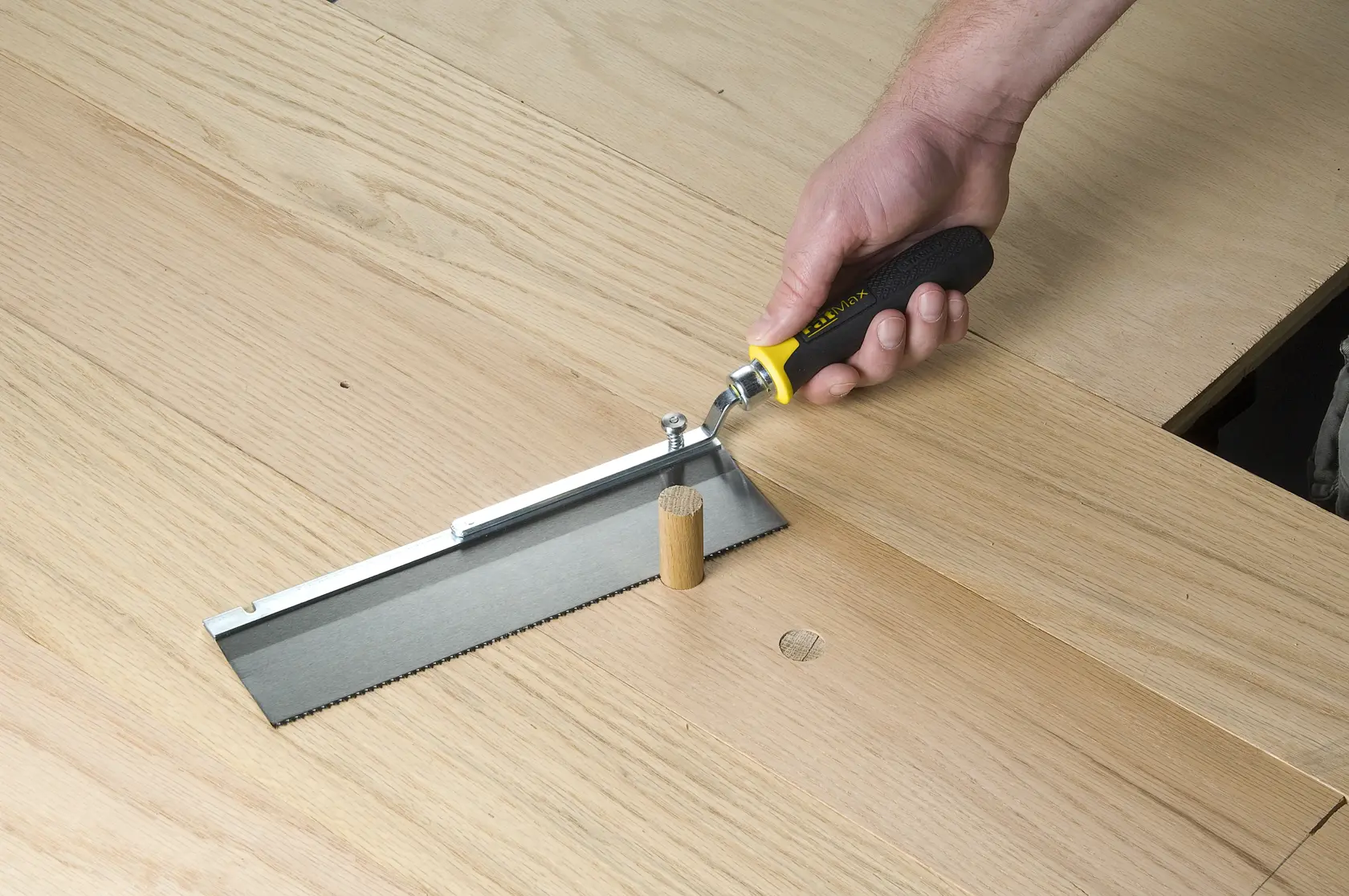 STANLEY 0-15-252 flush cut saw with black and yellow handle trimming a wooden dowel on a light wood surface.