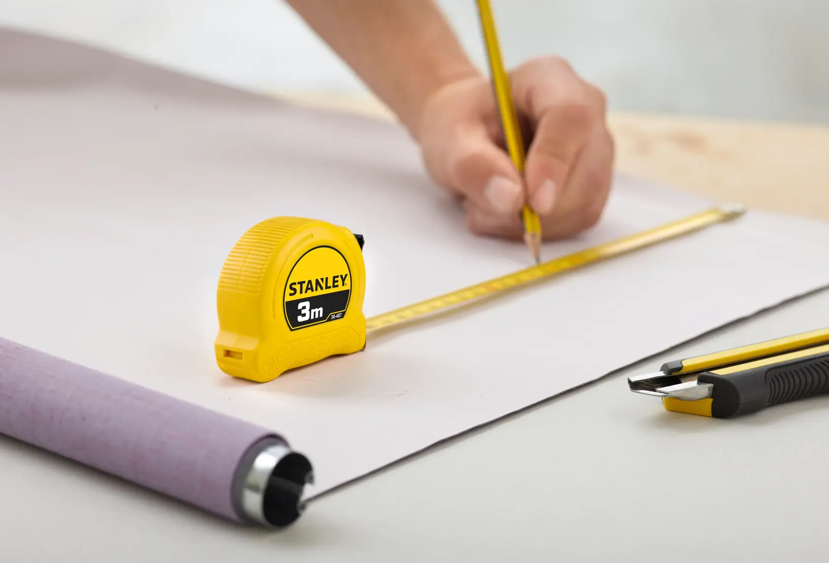 STANLEY 0-30-487 tape measure, 3m, yellow body, used for measuring on desk with pencil and cutter.