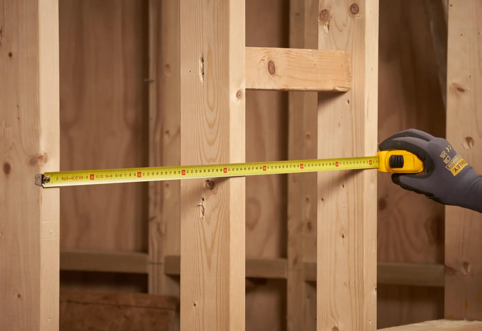 STANLEY 0-30-497 tape measure extended between wooden studs, close-up side view.