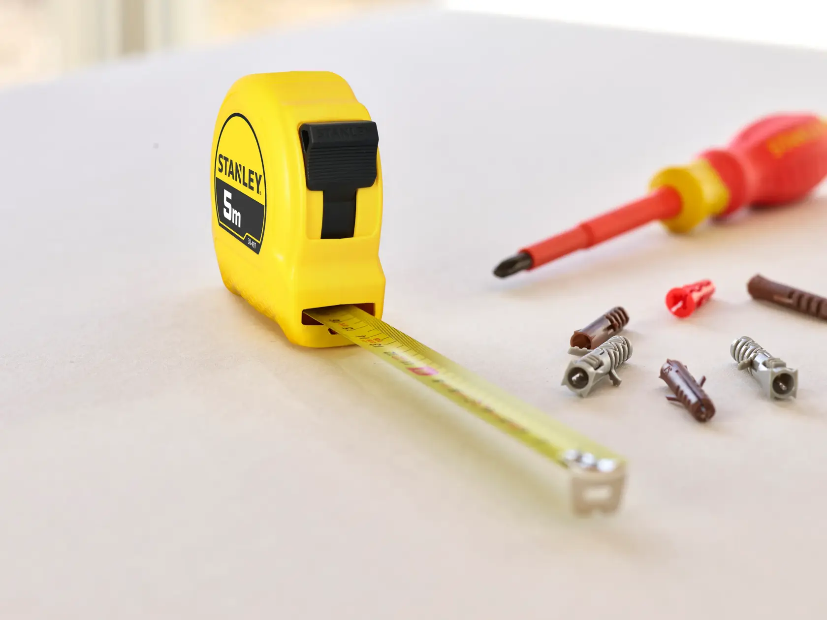 STANLEY 0-30-497 tape measure with yellow casing, extended blade, screwdriver and fasteners on flat surface.
