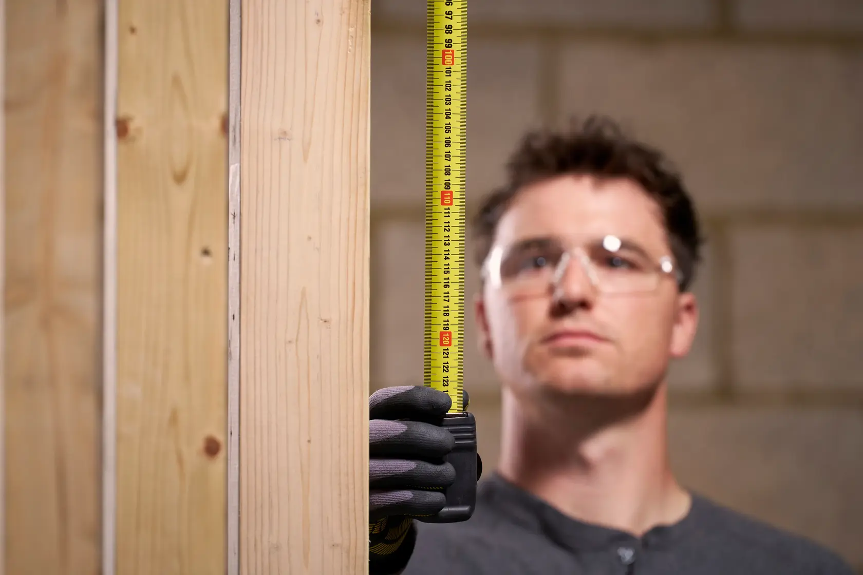 STANLEY 0-33-728 tape measure held vertically by gloved hand, measuring wooden beam, photography close-up.