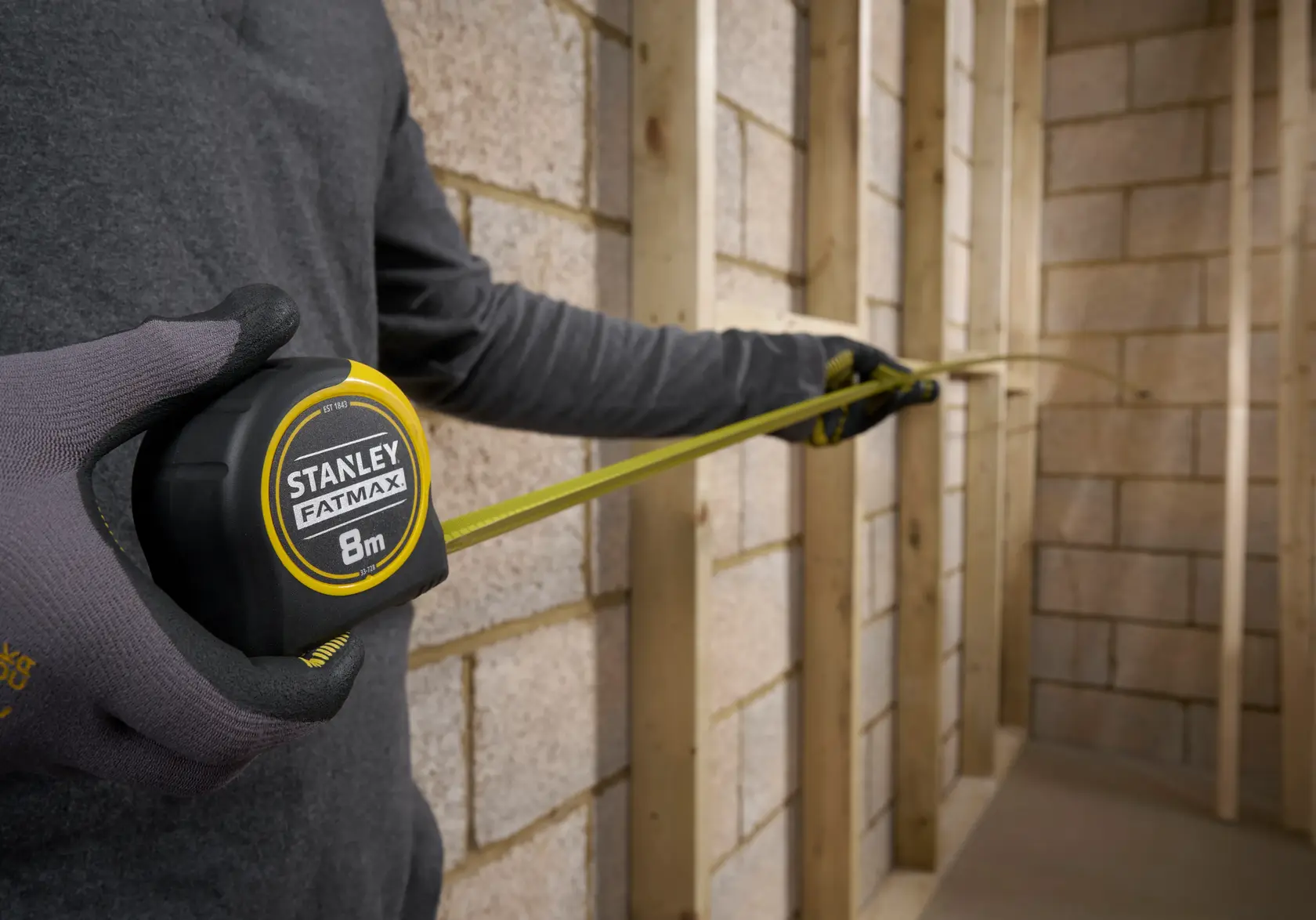 STANLEY 0-33-728 tape measure in use, yellow blade extended inside framed wall, FATMAX branding visible.