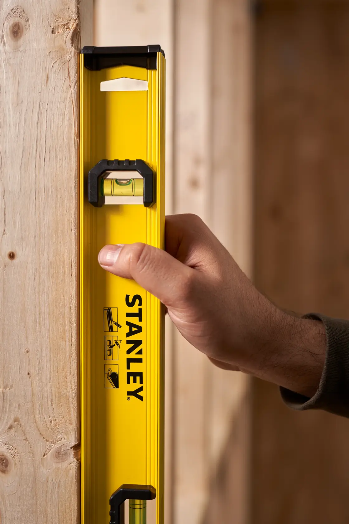 STANLEY 0-42-074 yellow spirit level held vertically against wooden beam, product photography.