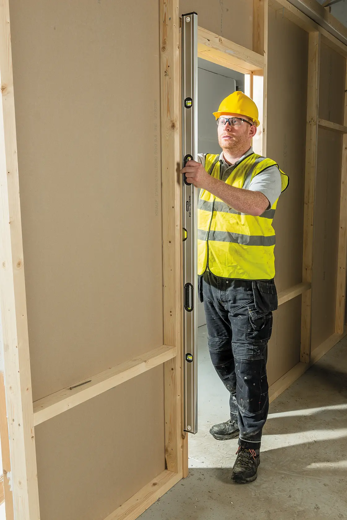 STANLEY 0-43-672 spirit level used vertically by worker in safety gear at wooden door frame on construction site.