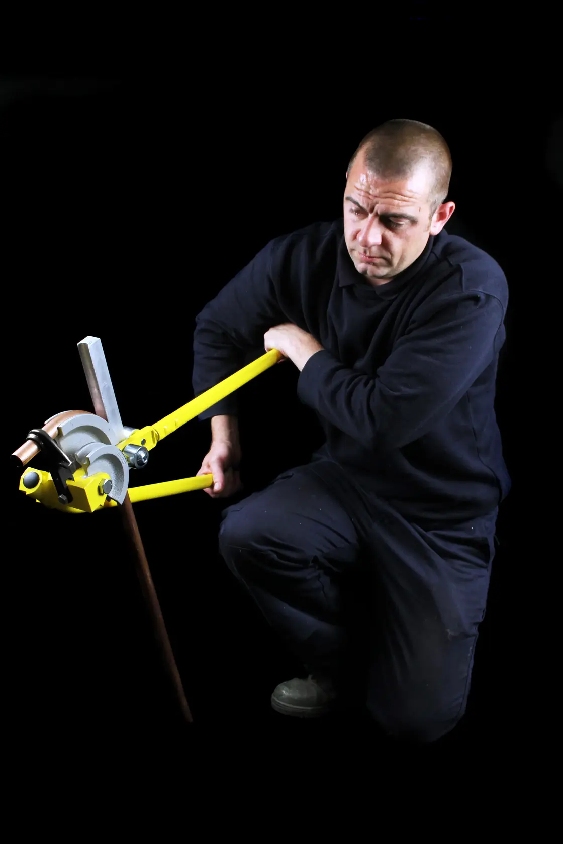 STANLEY 0-70-452 pipe bender in use, yellow handles, bending copper pipe, shown against black background.