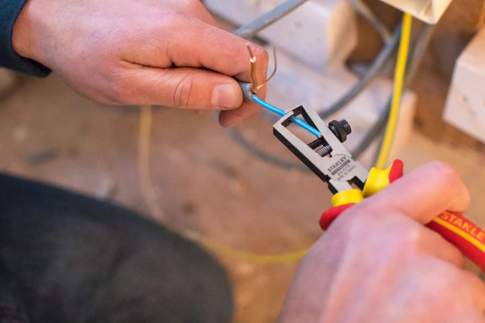 STANLEY 0-84-010 wire stripper in use, stripping blue electrical wire during installation.