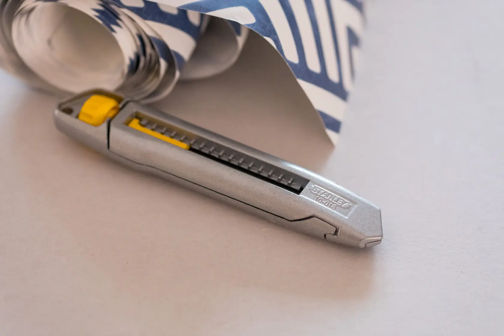 STANLEY 1-10-018 Universalmesser mit silbernem Gehäuse und gelbem Schieber, neben gemustertem Papier.