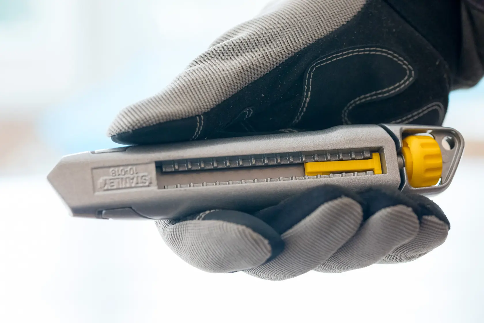 STANLEY 1-10-018 Universalmesser in Grau und Gelb, gehalten mit Handschuh, Seitenansicht.