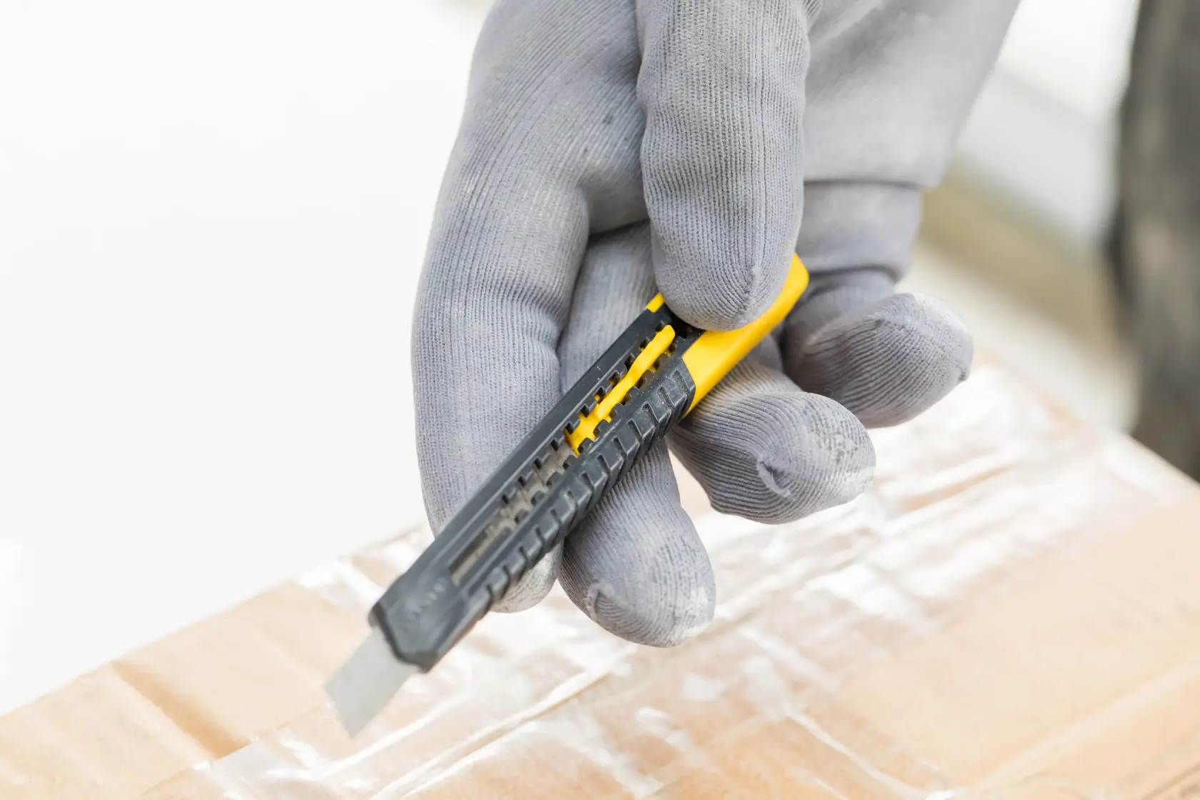 Foto von STANLEY 1-10-150 Universalmesser in behandschuhter Hand beim Schneiden von Karton, Nahaufnahme.
