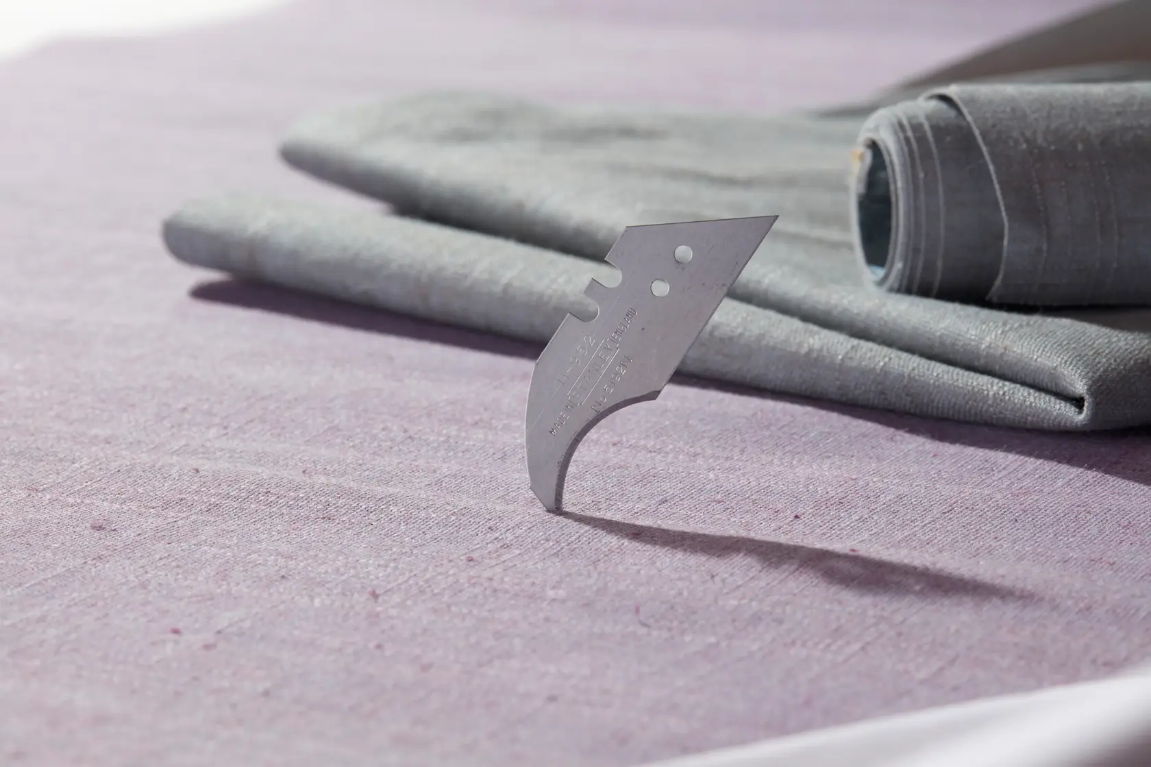 STANLEY 1-11-952 curved carpet blade standing upright on fabric, close-up side angle photography.