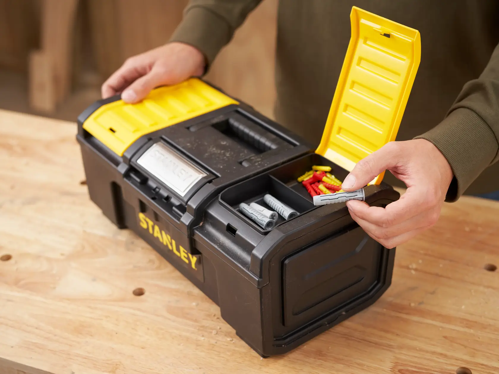 STANLEY 1-79-216 black and yellow toolbox with open lid, showing compartments holding wall plugs on a workbench.