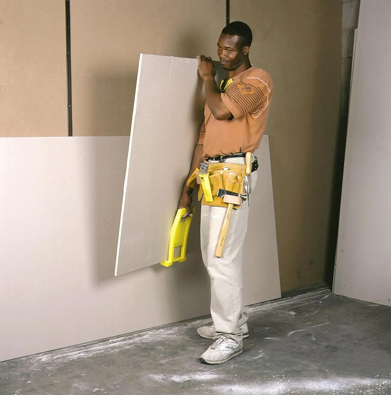 STANLEY 1-93-301 drywall carrier tool held by worker with tool belt, standing next to drywall sheets.