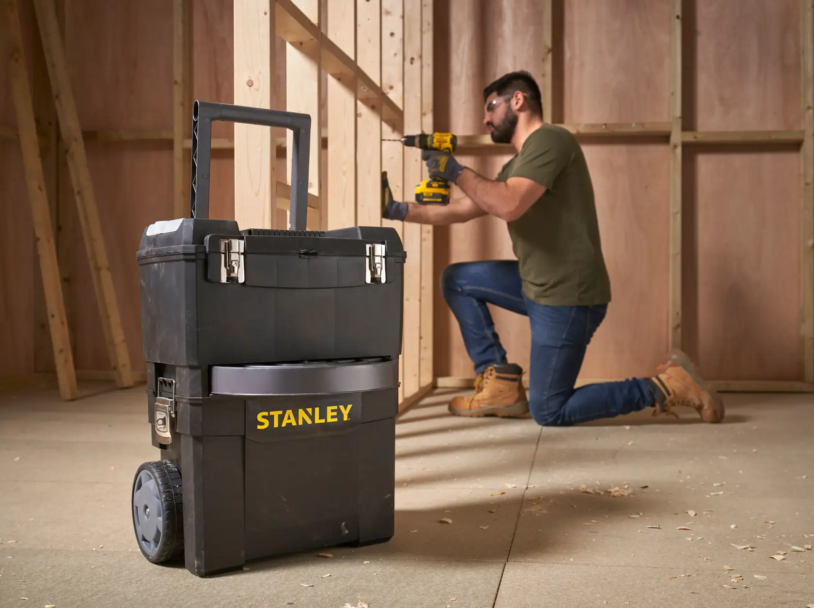 STANLEY 1-93-968 mobiler Werkzeugkasten mit Rädern in Werkstatt, Arbeiter nutzt Elektrowerkzeug im Hintergrund.