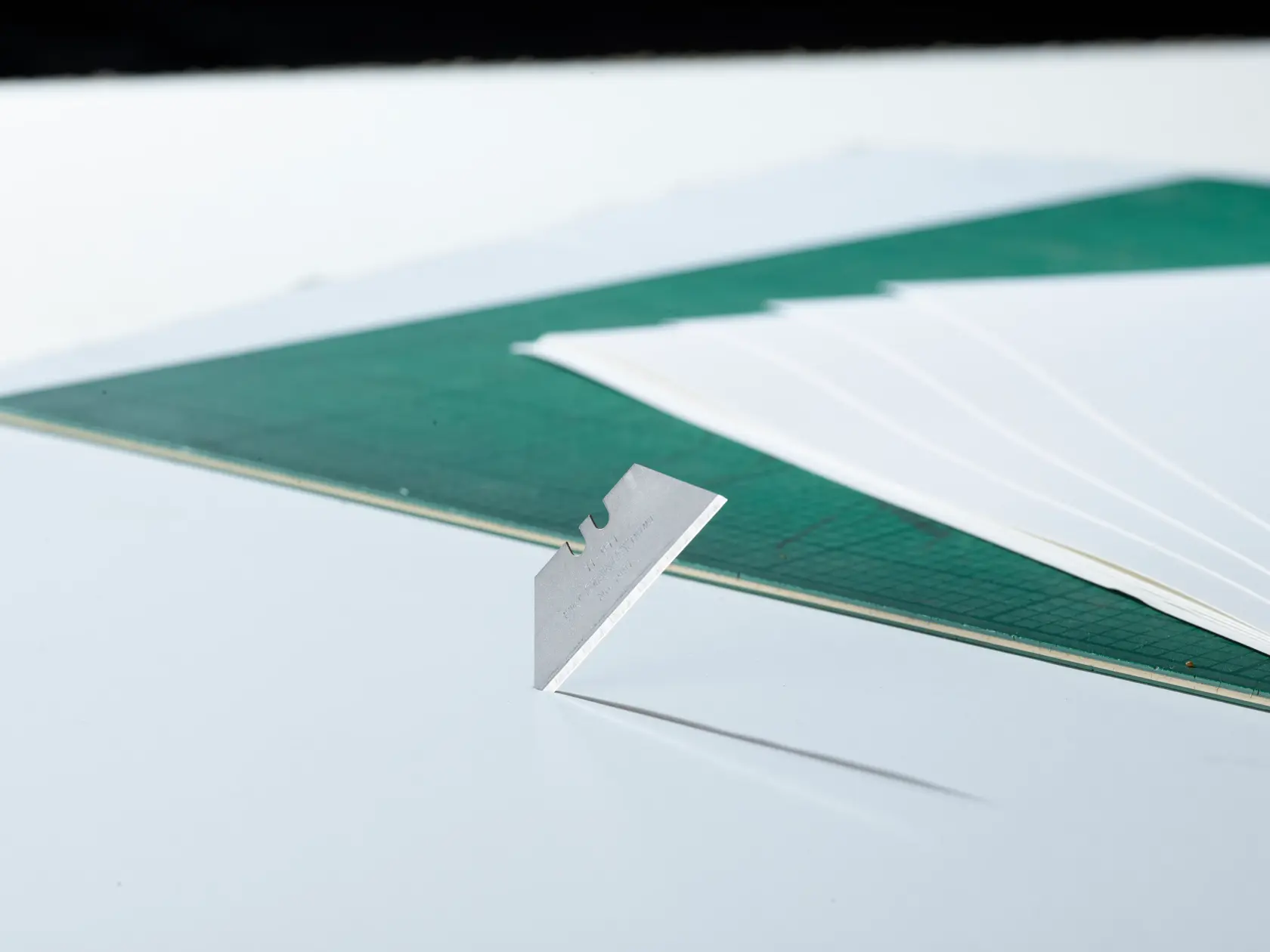 STANLEY 2-11-911 utility blade upright on white surface, green cutting mat and papers in background.