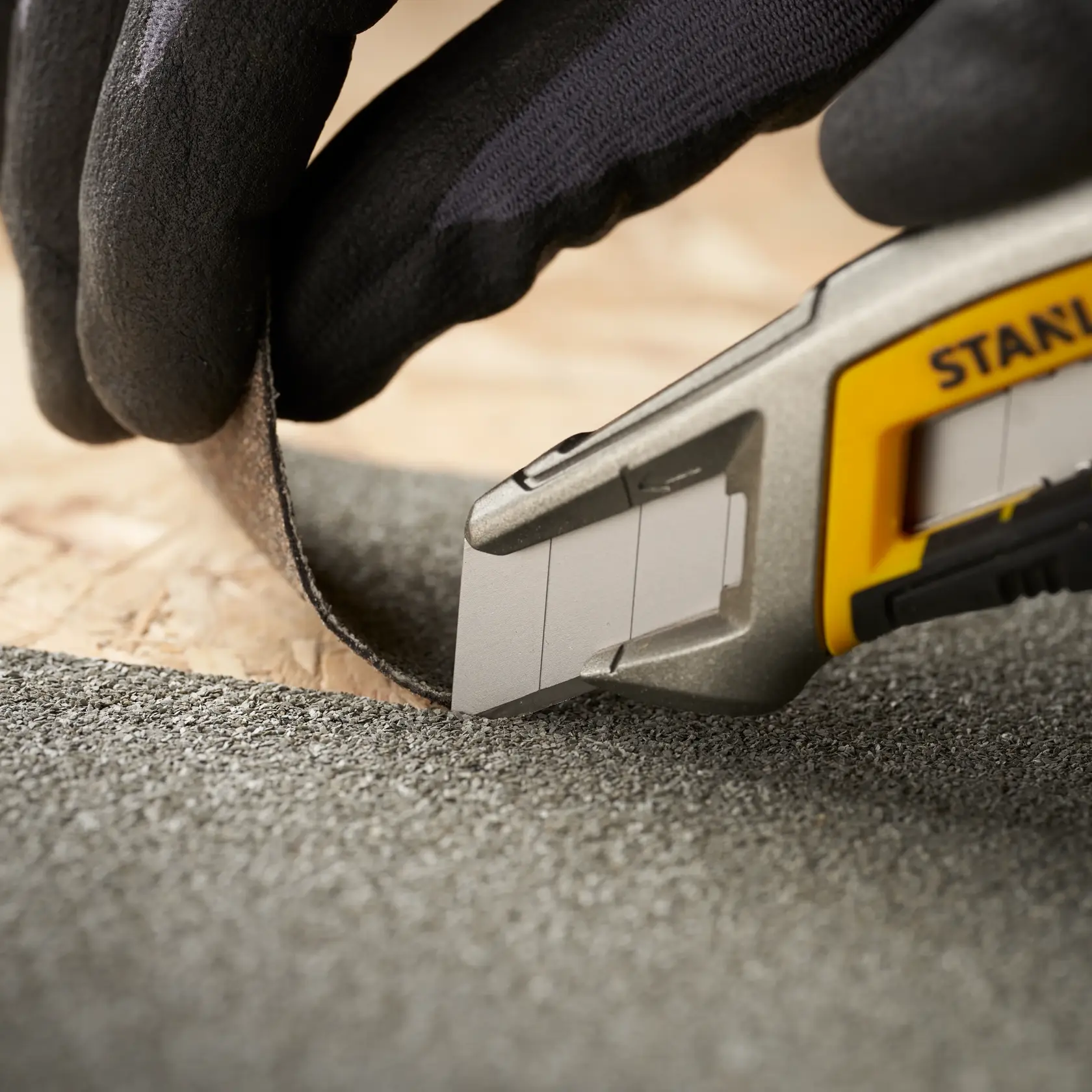 STANLEY 3-11-301 utility knife cutting roofing material, close-up angle, with gloved hand holding material.