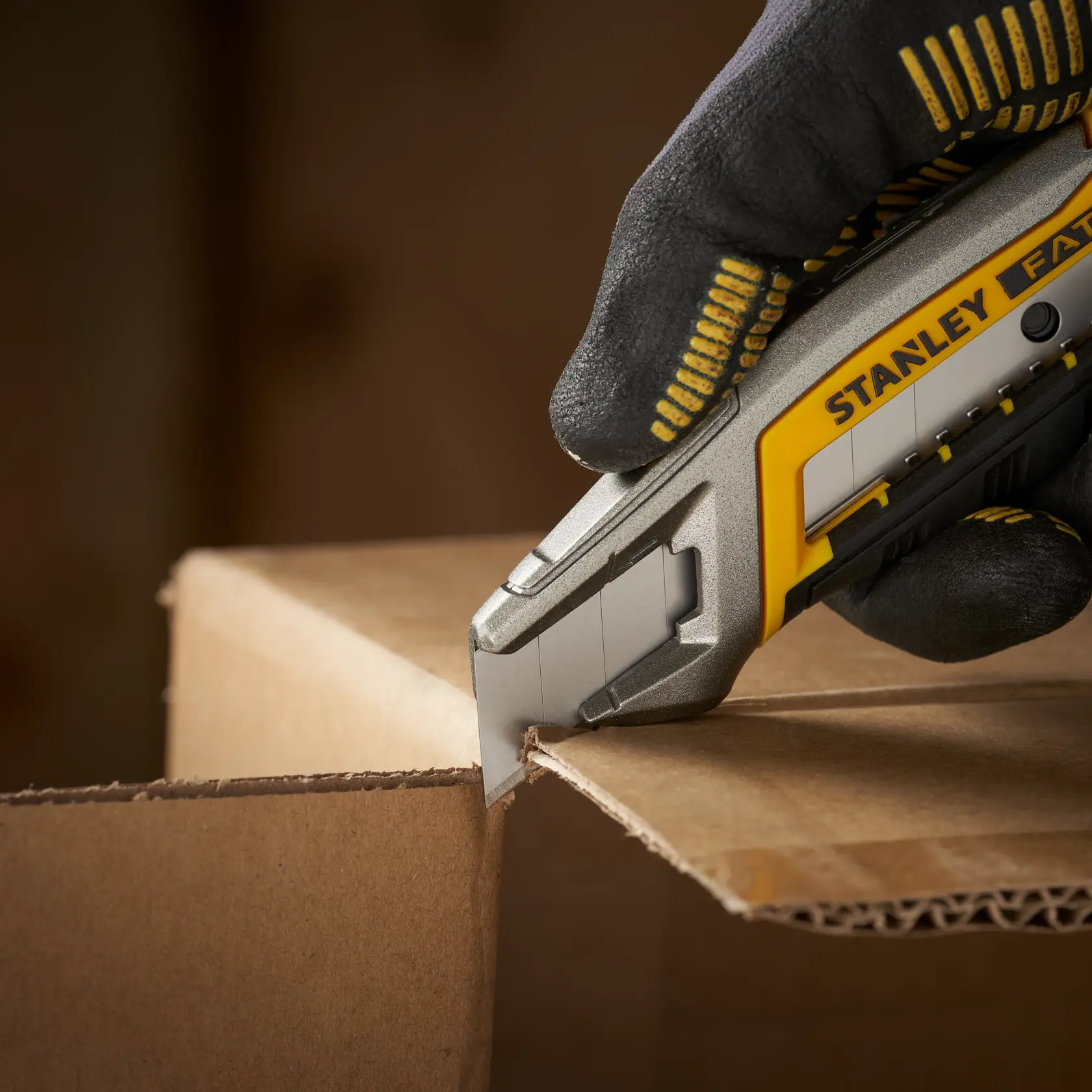 STANLEY 3-11-301 utility knife cutting cardboard, close-up, hand with glove holding the tool.