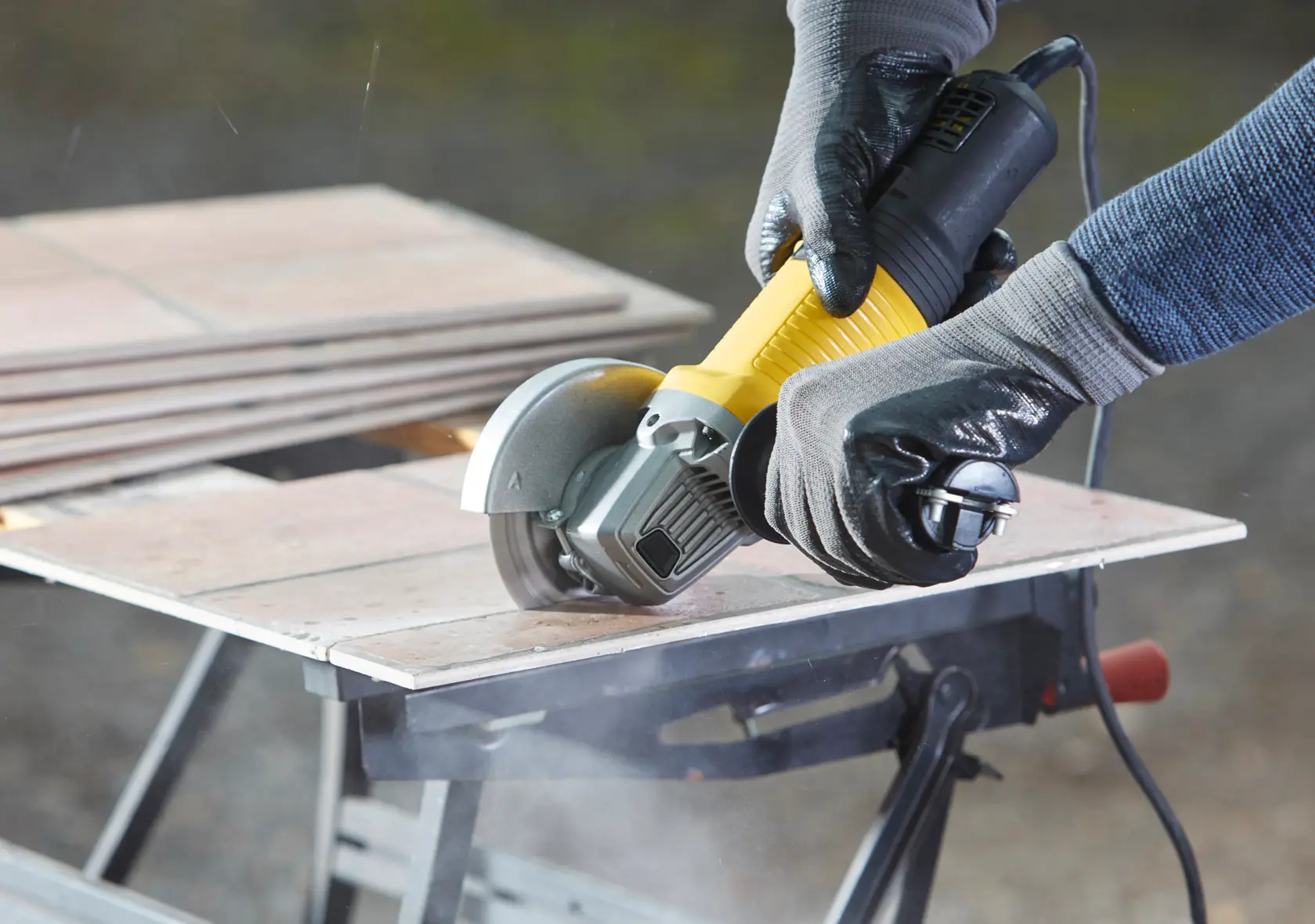 Photo of STANLEY FMEG220K angle grinder cutting ceramic tile on a workbench, close-up side view.