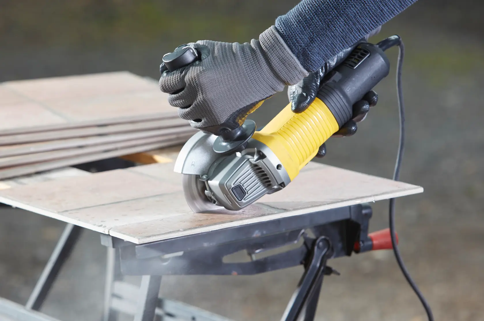 Photo of STANLEY FMEG220K angle grinder cutting ceramic tiles on a workbench.