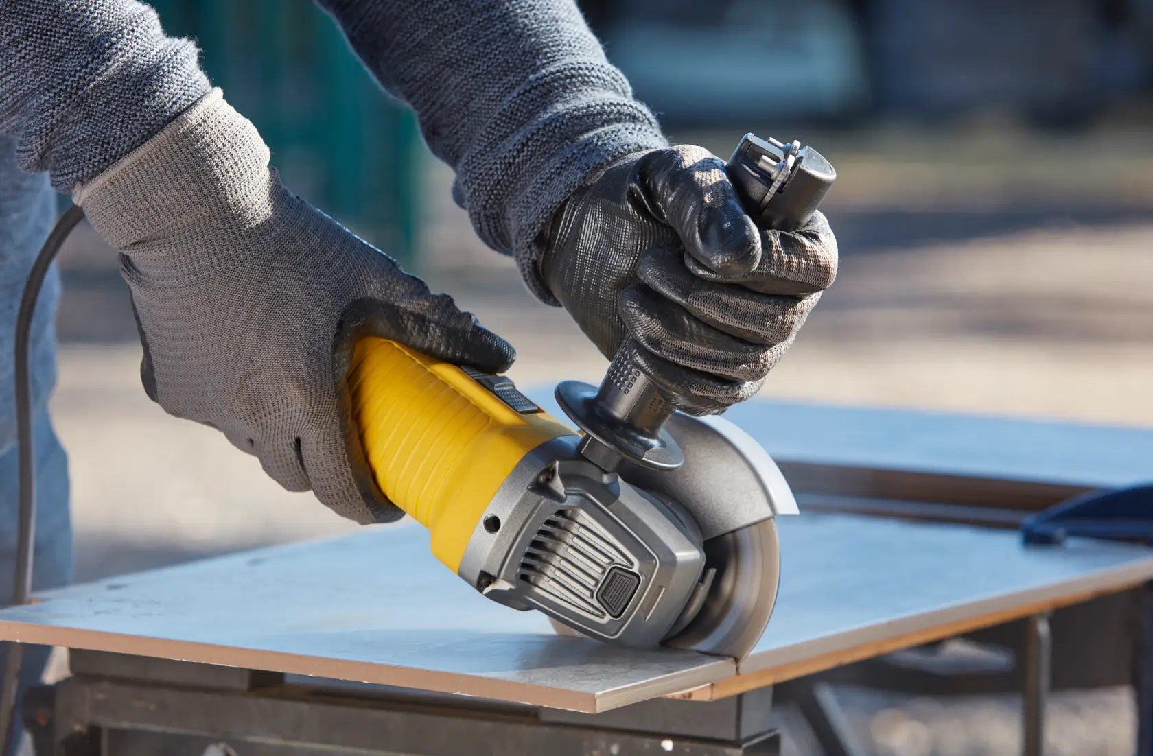 STANLEY FMEG220K angle grinder cutting tile, close-up of hands in gloves outdoors.