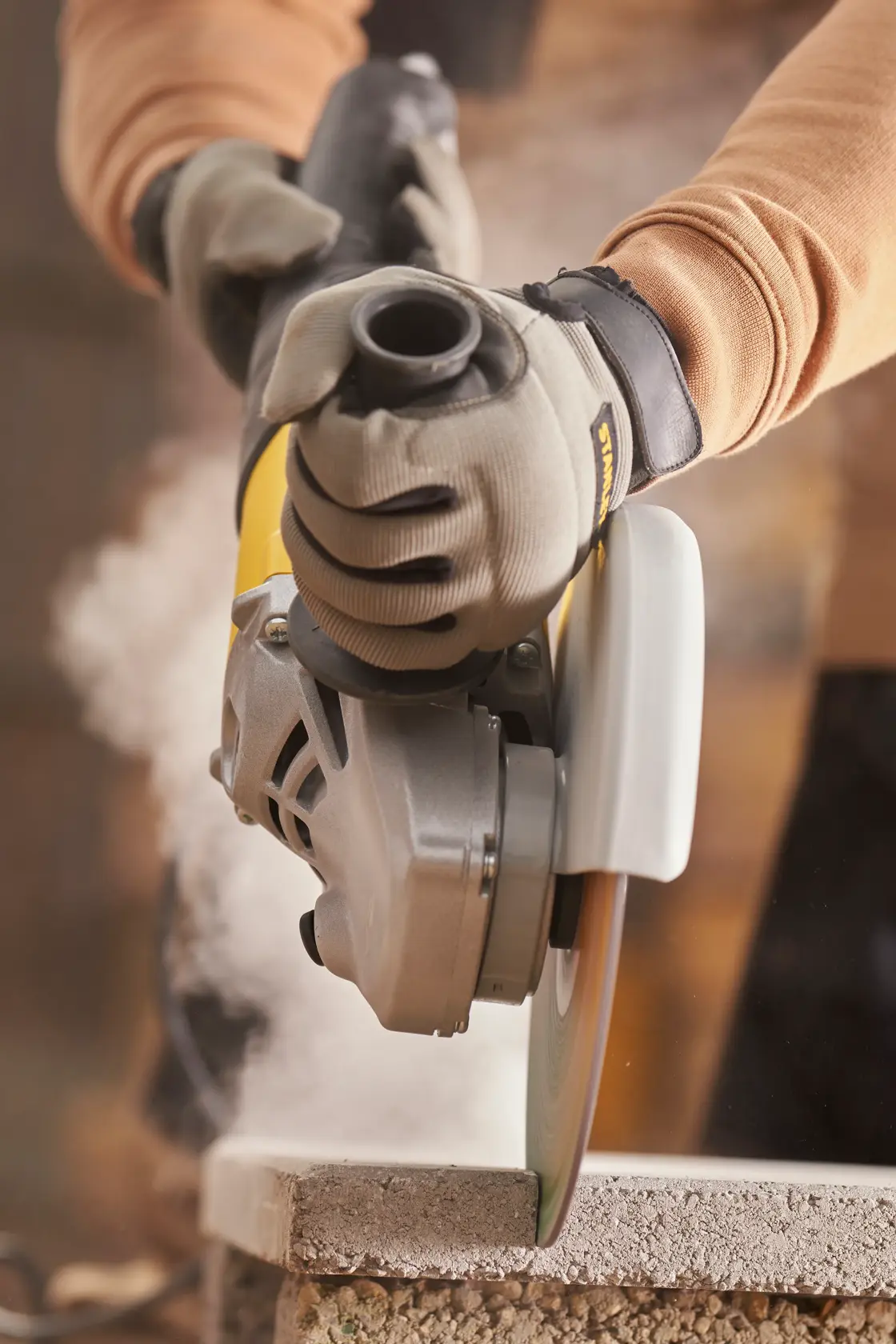 STANLEY FMEG232 angle grinder in use cutting concrete, close-up side view, worker wearing gloves.
