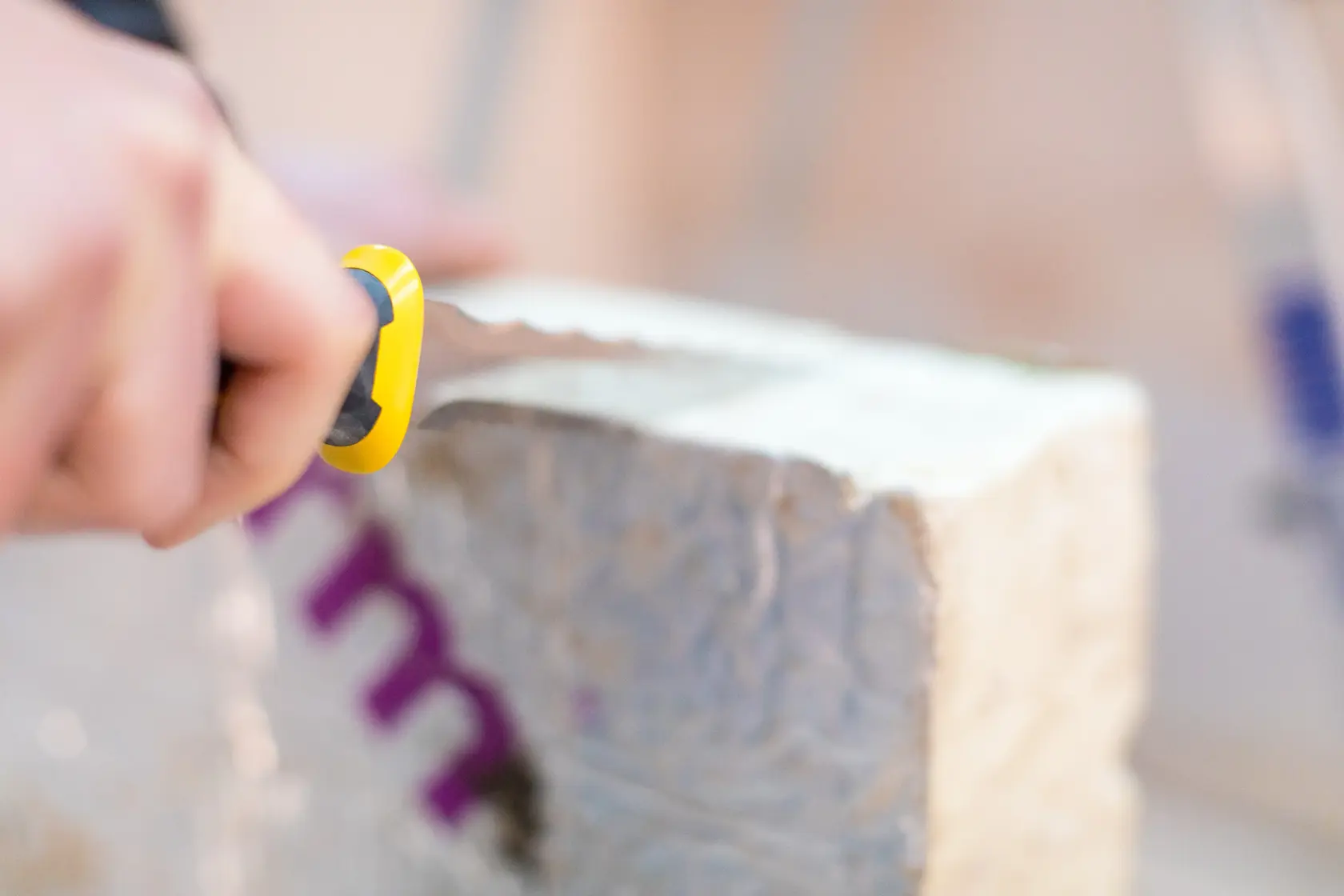 Photo of STANLEY FMHT0-10327 utility knife cutting insulation block, close-up view.