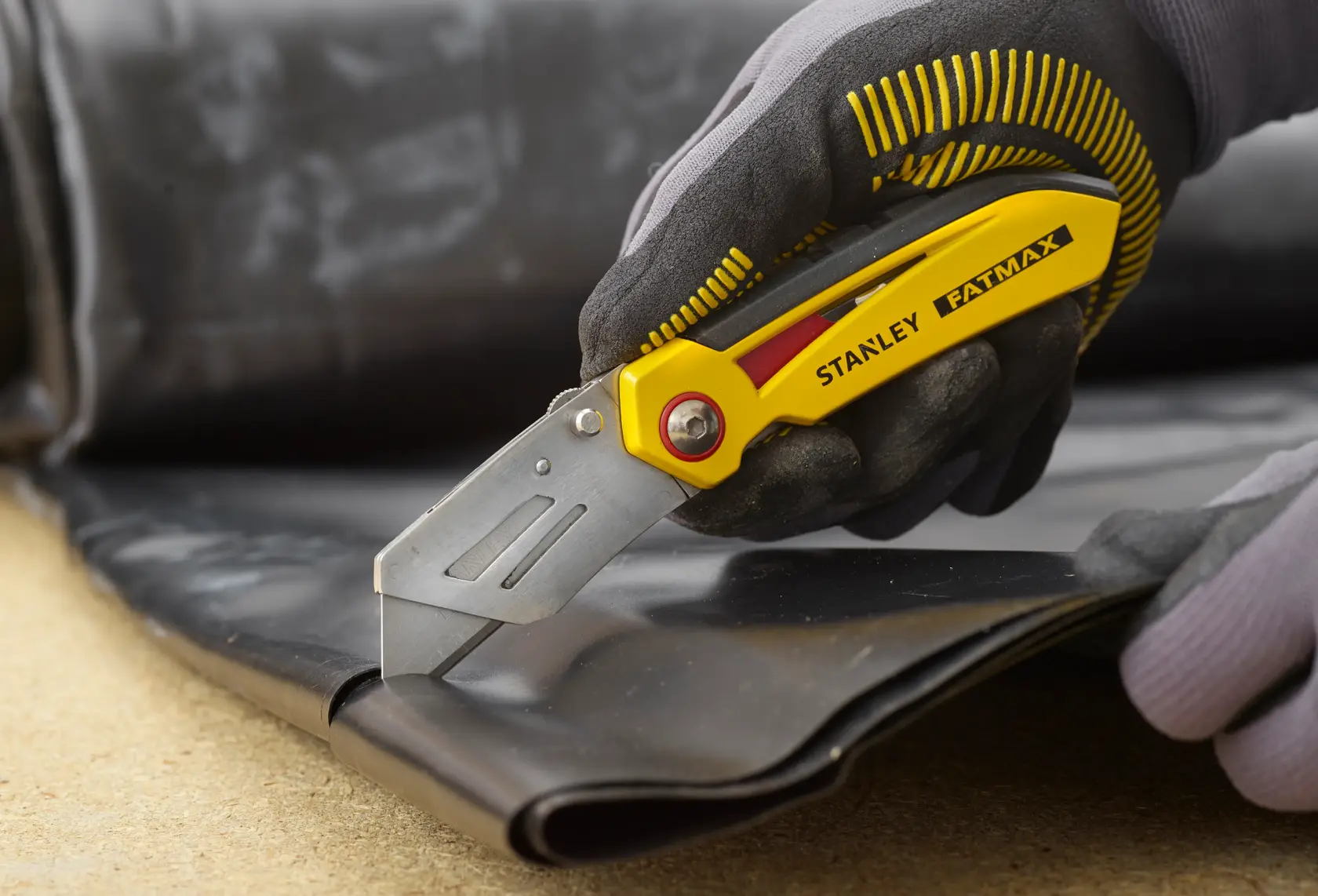Stanley FMHT0-10827 utility knife cutting black material, close-up view, yellow and silver design.