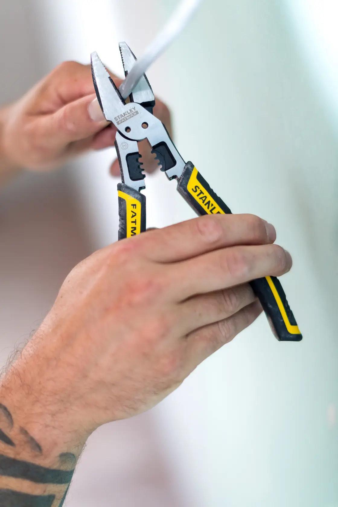 Stanley FMHT0-75469 pliers with black and yellow handles stripping wire, close-up in use.