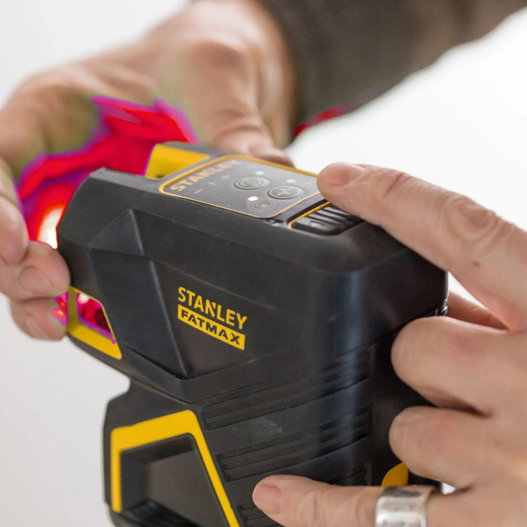 STANLEY SKU FMHT1-77414 FATMAX laser level, close-up photography, black and yellow housing, hands interacting.