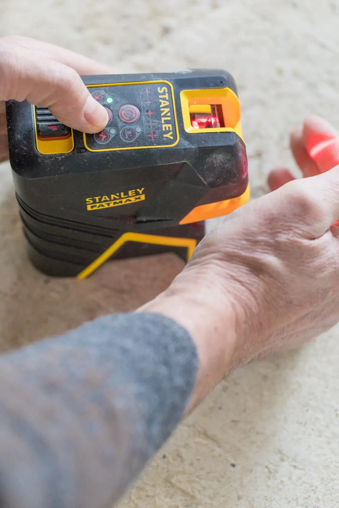 Photo of STANLEY FMHT1-77415 laser level tool in use, close-up of hands operating the black and yellow device.