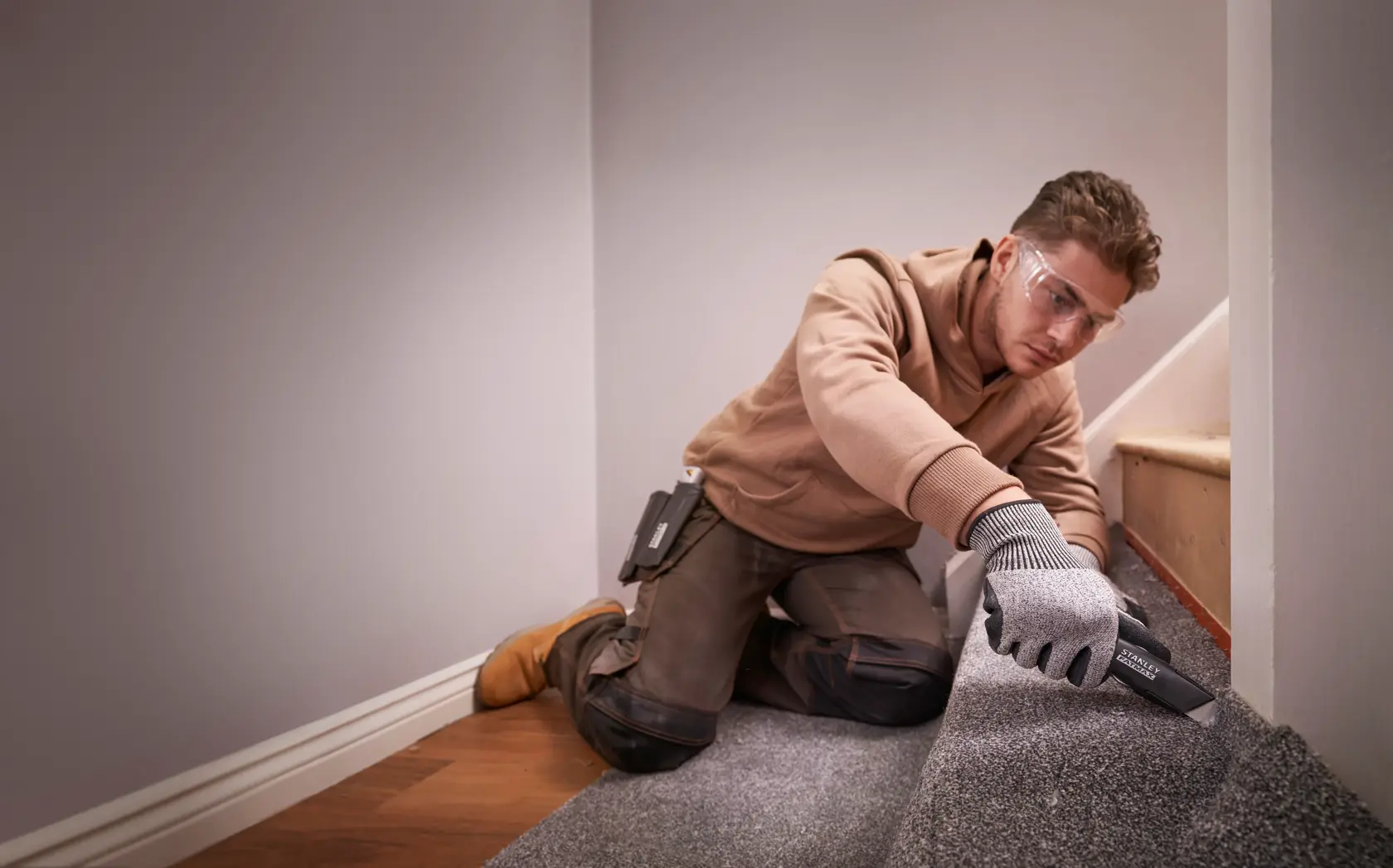 Foto eines Arbeiters, der mit dem STANLEY FMHT10500-0 Universalmesser Teppich auf einer Treppe schneidet, mit Handschuhen und Arbeitskleidung.