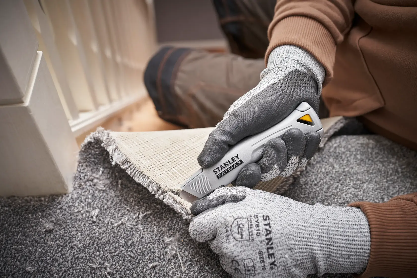 STANLEY FMHT10501-0 Universalmesser schneidet Teppich, Nahaufnahme des Einsatzes mit Handschuhen.
