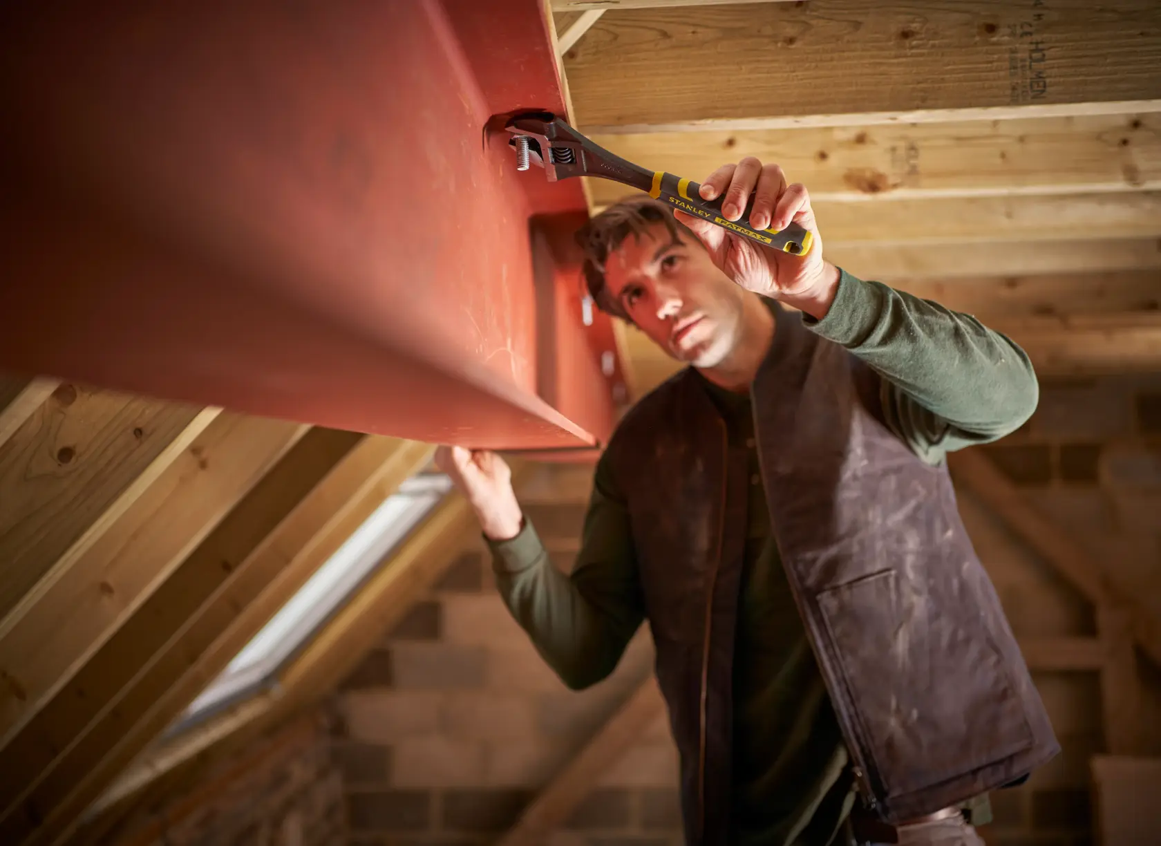 STANLEY FMHT13126-0 adjustable wrench used by a worker on a metal beam in an attic, action photo.