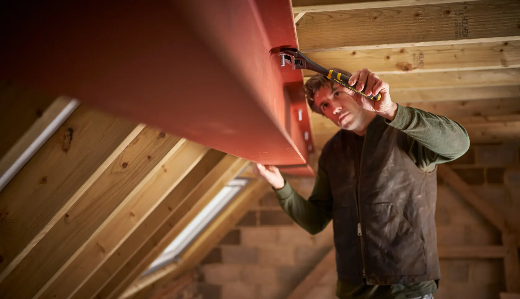 Photo of STANLEY FMHT13128-0 pliers in use tightening a bolt on a red steel beam in a wooden attic.