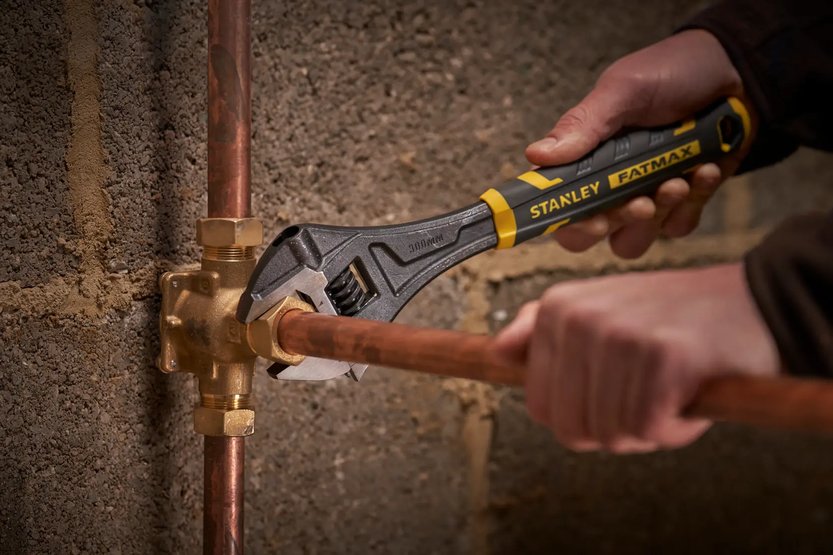 STANLEY FMHT13128-0 adjustable wrench turning pipe fitting against concrete wall.