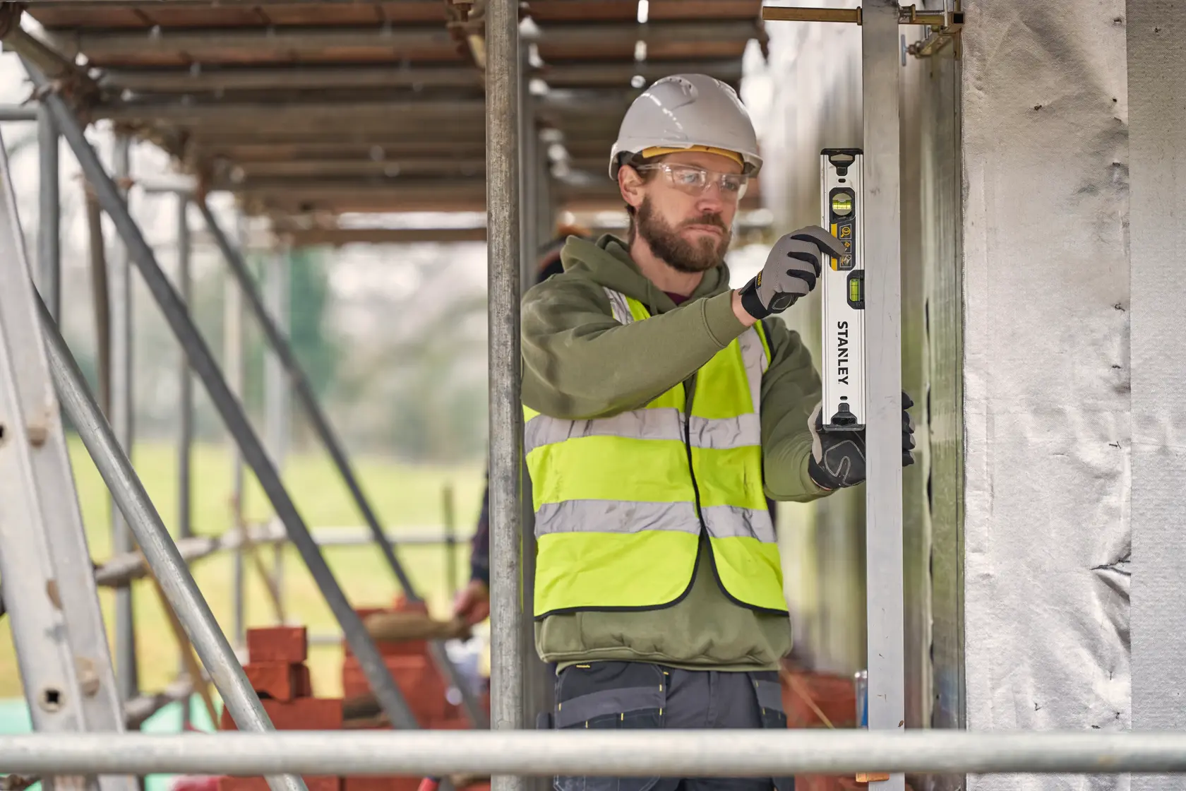 Worker using STANLEY FMHT43670-1 spirit level at construction site wearing safety vest and helmet.