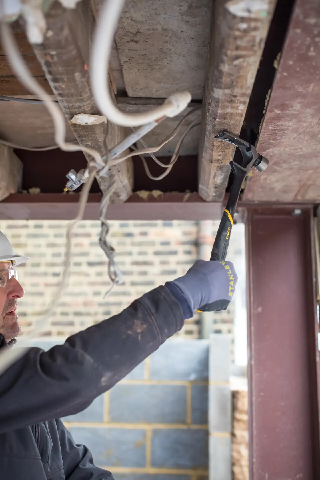 Photo of STANLEY FMHT51367-2 hammer in use for demolition under a ceiling, visible gloved hand holding the tool.