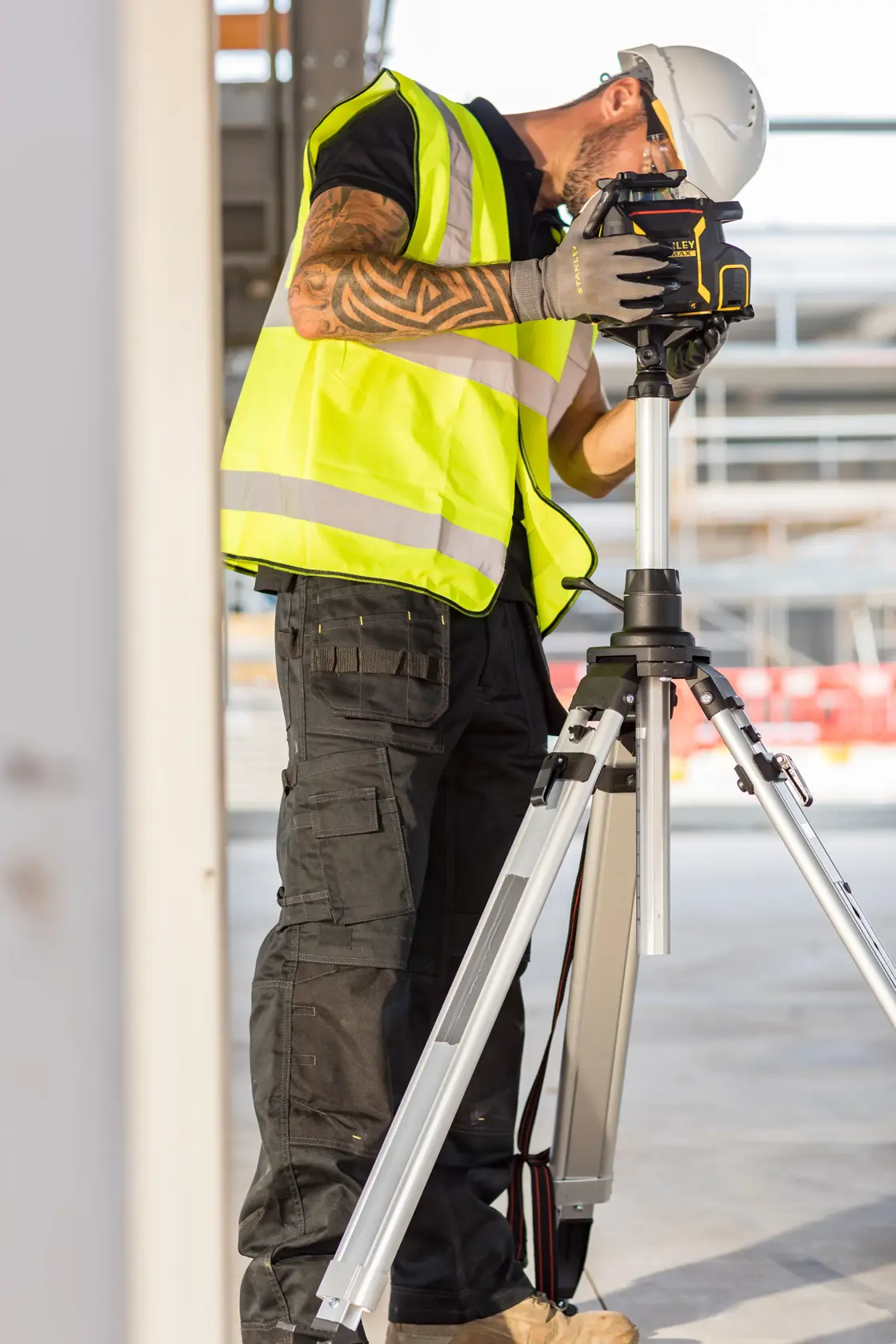 STANLEY FMHT77449-1 construction laser level on tripod, used by worker in safety vest and helmet.