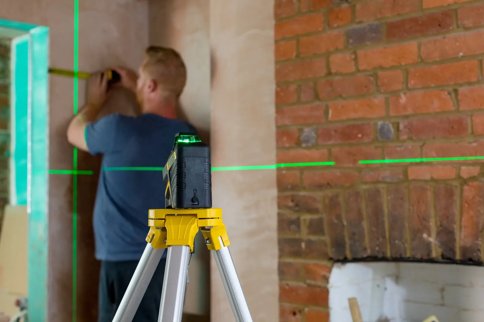 STANLEY FMHT77617-1 laser level on tripod projecting green lines, used for interior wall measurement.